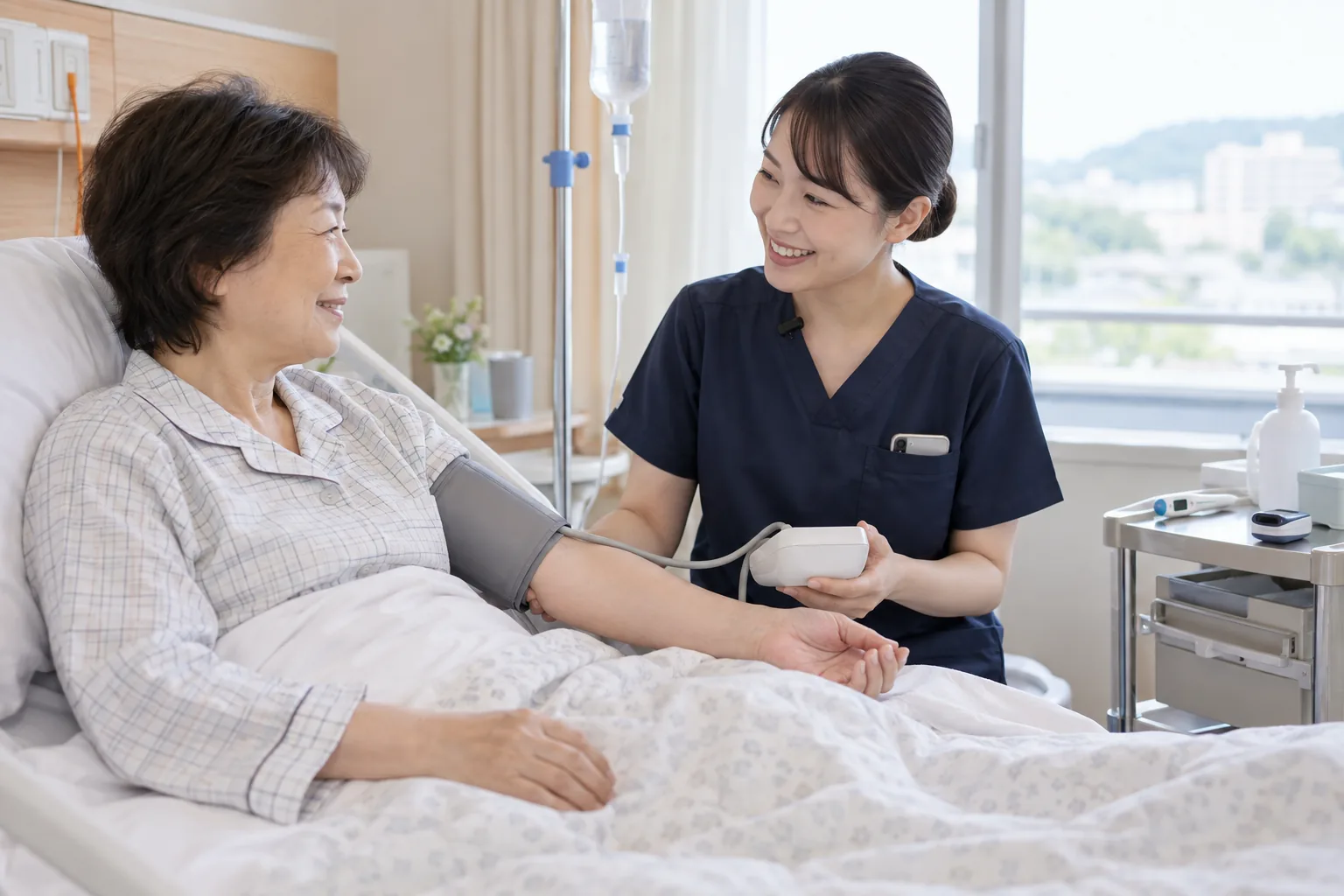 病室で、看護師が入院着の患者さんの血圧を測りながら話しかけている。看護師の襟にワイヤレスマイク、胸ポケットに院内スマホ